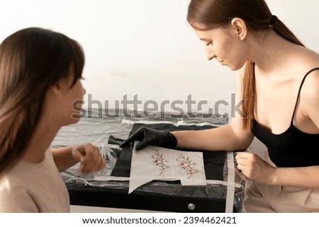 female tottooist showing sketch of a tattoo to her client in the office 