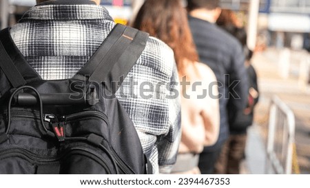 Close-up at back of a man with backpack bag during queue up and waiting to buy a attractive event ticket, with blurred background of many people in queue. Royalty-Free Stock Photo #2394467353