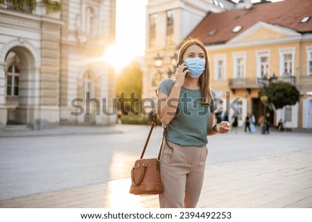 Cropped shot of beautiful businesswoman talking on the phone while wearing face mask outdoors.