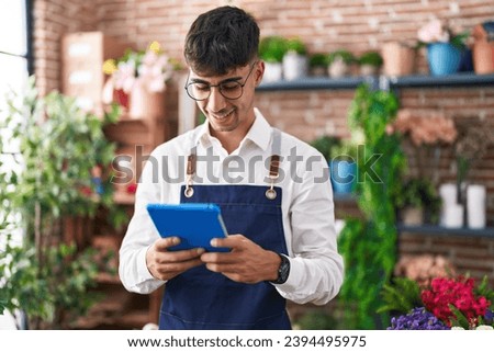 Young hispanic man florist smiling confident using touchpad at florist