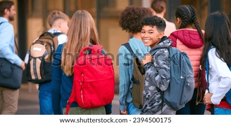 Portrait Of Male Secondary Or High School Student Outside School Building With Teachers And Pupils Royalty-Free Stock Photo #2394500175