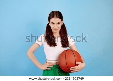 Young brunette teenage girl with basket ball and ponytails on blue background.