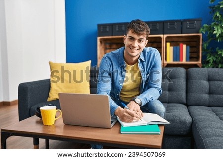 Young hispanic man student sitting on sofa writing on notebook at home