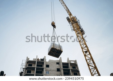 A crane lifts bricks to a height for the construction of a high-rise building. photograph of a construction site against a blue sky