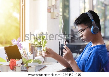 Asian schoolboy doing homework at home by learning various leaves and flowers by using magnifying glass and laptop, now he is learning about cos leaf and green oak leaf for salad menu of healthy food.