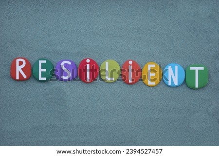 Resilient, someone able to withstand or recover quickly from difficult conditions, creative text composed with hand painted multi colored stone letters over green sand