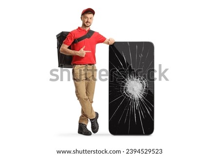 Delivery man leaning on a smartphone with a broken screen and pointing isolated on white background