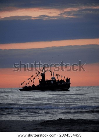 This picture captures a tourist ship sailing on the sea during a sunset. The orange sky and small waves create a serene atmosphere. The horizon and the setting sun are visible in the background.