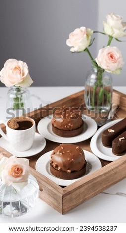Elegant photo of luxurious, artisanal desserts: chocolate tartlets and mousse pastries on white plates, artfully arranged on a wooden tray with coffee and live roses in small vases Royalty-Free Stock Photo #2394538237