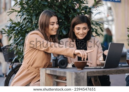 Female photographer checking pictures on camera with her client. Women sitting in cafe and drinking coffee. Work space outdoors