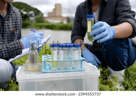 Environmental Engineers Inspect Water Quality, pH Test and Take Water sample notes in The Field Near Farmland, Fish Pond, Natural Water Sources that may be Contaminated by Suspicious Pollution Sites. Royalty-Free Stock Photo #2394555737