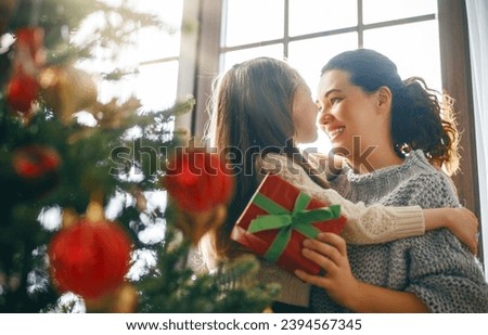 Merry Christmas and Happy Holidays. Cheerful mom and her cute daughter girl exchanging gifts. Parent and little child having fun near tree indoors.