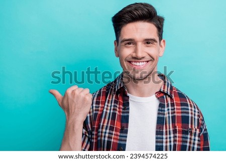 Photo of charming toothy guy wear checkered shirt pointing thumb empty space isolated blue teal color background