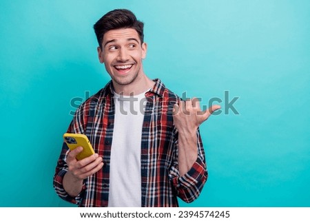 Photo of charming excited guy wear checkered shirt gamling modern gadget thumb empty space isolated blue teal color background