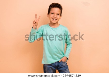 Photo of cheerful positive boy wear trendy clothes showing v-sign have fun good mood isolated on beige color background