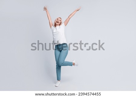 Full length photo of optimistic girl dressed white t-shirt denim pants rasing hands up look empty space isolated on gray color background Royalty-Free Stock Photo #2394574455