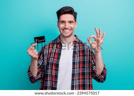Photo of good mood positive guy wear checkered shirt holding credit card showing okey gesture isolated blue teal color background