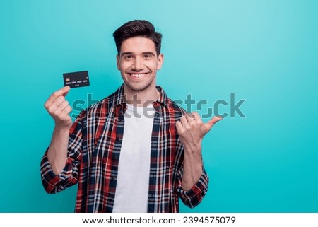 Photo of funky good mood guy wear checkered shirt holding credit card thumb empty space isolated blue teal color background