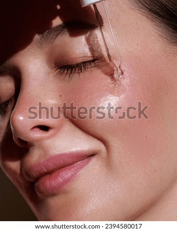 Serum. Moisturising and nourishing.  Close up beauty portrait of  beautiful woman with glowing skin is applying a vitamin c skincare product with a pipette dropper.  Royalty-Free Stock Photo #2394580017