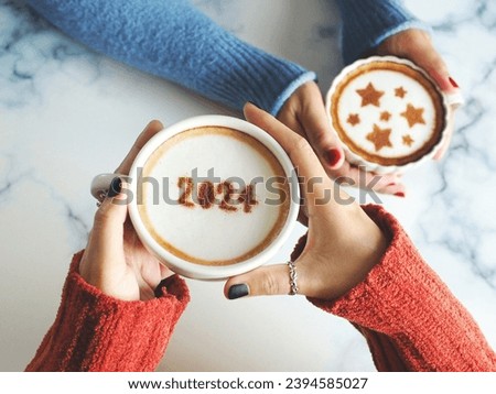 Coffee cup with the number 2024 on frothy surface in female hands holding over white marble table and another one with blurred star symbols on frothy surface. Happy new year 2024 food art theme. Royalty-Free Stock Photo #2394585027