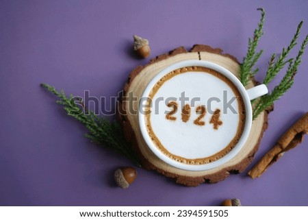 Happy New Year 2024 theme coffee cup with number 2024 over frothy surface served on wooden plate over purple violet background with green pine branches, red oak acorns and cinnamon stick.
