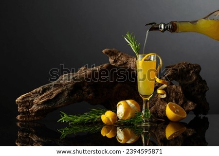 Traditional Italian liqueur Limoncello on a black reflective background. Glass of lemon liquor with rosemary twig on a background of old snag. Liquor is poured into a glass. Royalty-Free Stock Photo #2394595871
