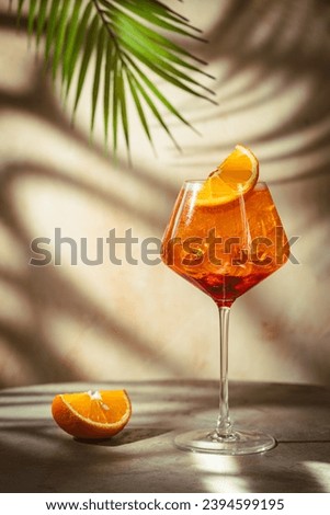 Glass of Aperol spritz cocktail with fresh oranges and palm leaves on beige background. natural light and shadows Royalty-Free Stock Photo #2394599195