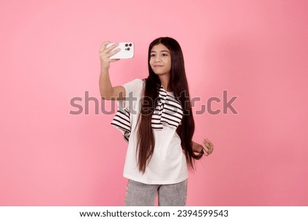 Young smiling teenage girl taking a selfie with phone on pink background in studio.