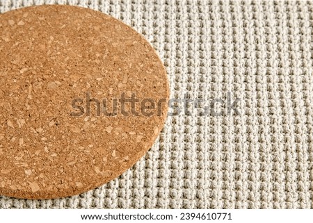 A fragment of a round beige cork coaster on a rough knitted tablecloth. Food menu template.