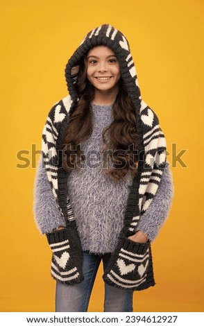 Teenager girl with winter hat over isolated yellow background. Winter christmas holidays, new year mood. Kids warm clothes. Warm hat with hood and scarf.