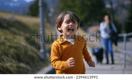 Joyful excited little boy running outside during autumn day wearing yellow pullover. Close-up face of child in motion sprinting forward feeling carefree Royalty-Free Stock Photo #2394613991