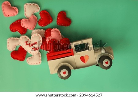 Valentine's Day hearts pillows white pink and red. All spilling out of a overturned truck. White toy truck with hearts on the doors and the wheels. On a teal background. Flat lay photography.  