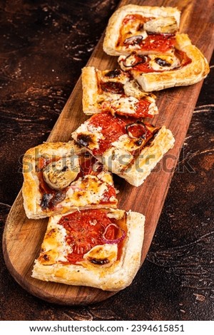 Baked Puff pastry tart pizza with artichoke, mozzarella, tomatoes and cheese sliced on a wooden board. Dark background. Top view.