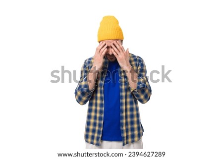 young pensive smart European brunette man with a beard and mustache is dressed in a yellow hat and blue shirt on a white background with copy space