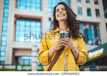 Beautiful happy young woman messaging on smartphone on the background of a city street on a sunny day. Business woman is looking away and smiling. She is standing in the city with a smartphone Royalty-Free Stock Photo #2394629423