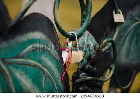 A heart-shaped steel padlock hangs on a fence with a ribbon, closed by the bride and groom. Wedding photography, symbol of love, Ukrainian traditions.