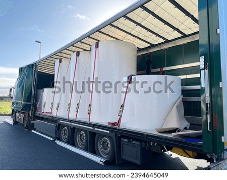 Loading, transporting and unloading large rolls of paper in a semi-trailer. Securing cargo with straps and locks for stability Royalty-Free Stock Photo #2394645049