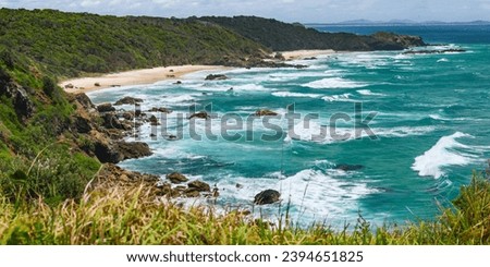 Australian coast, view from a cliff of the blue ocean and a rocky shore with a sandy beach. Small bay with volcanic rock, sunny day.