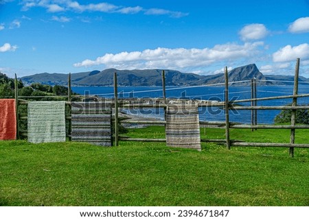 Realistic view from hill of classic carpet runners being dried on fence on northern fjords of Lofoten Islands.