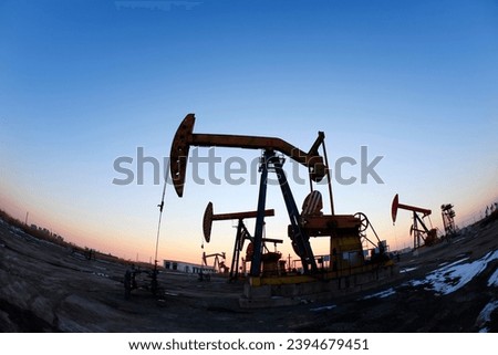 Oil field site, in the evening, oil pumps are running, Silhouette of beam pumping unit
