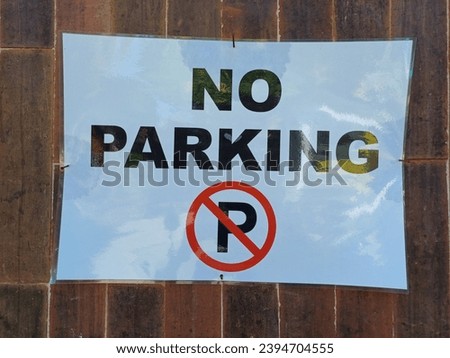 black printed writing with the letter p crossed in red printed on white paper laminated paper with no parking written on it displayed on the wall