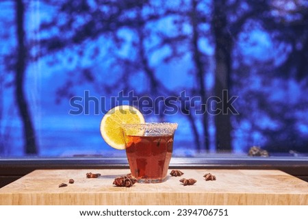 Glass of hot mulled wine or spiced wine in front of window during winter evening. Mulled wine is alcoholic drink usually served at Christmas markets in Europe, mainly in Germany, Austria, Switzerland. Royalty-Free Stock Photo #2394706751