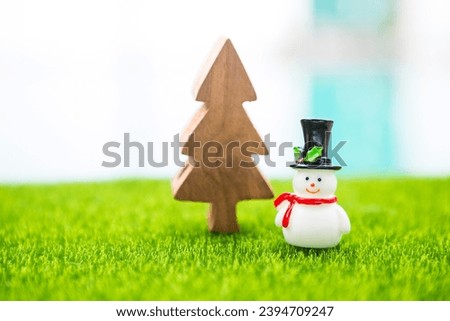 Simple Christmas card background idea, Snowman doll with wooden tree on green field over blurred background, outdoor day light 