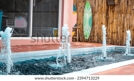 Picture of a small fountain in the pond in front of the glass room. There are 4 pumps in total. The water inside is bright blue. while the surface around the edge of the pool is brown.