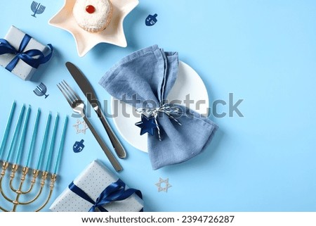 Jewish religious holiday Hanukkah table setting. Flat lay plate with napkin, cutlery, gift boxes, jelly donut on blue background.