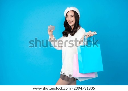 Young Asian woman with long hair, online business shopper, sideways, cute smile, holding credit card and smartphone. There are shopping bags. Wearing a coat to photograph a blue backdrop in a studio