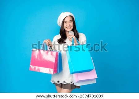 Young Asian woman shopping for online business using smartphone, long hair, wearing a white coat, beautiful smile, holding several shopping bags, taking photo, blue background in studio.
