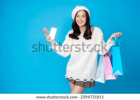 Half body photo of young Asian woman with long hair, online business shopper. Holding a credit card and a smartphone There are shopping bags. Wearing a coat to photograph a blue backdrop in a studio