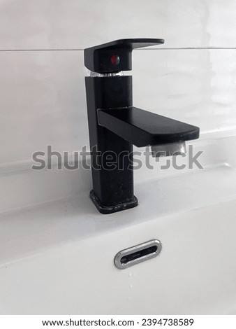 interior close up photo view of a design modern black water tap in a clean empty bathroom with a white sink and white tiles on the wall with nobody around