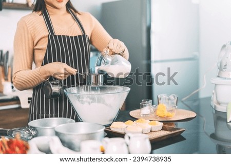 Woman hand pouring milk on measuring cup in glass bowl. Making cake at home kitchen concept. Royalty-Free Stock Photo #2394738935